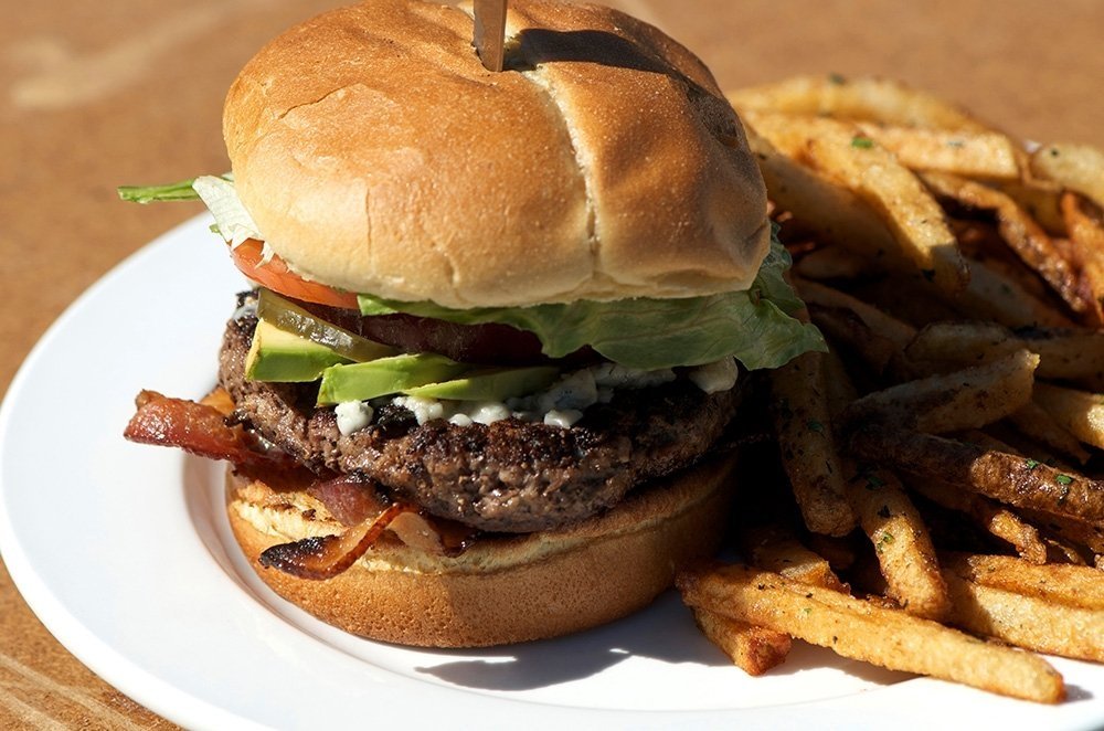 Burger with avacado and bacon on a plate with fries